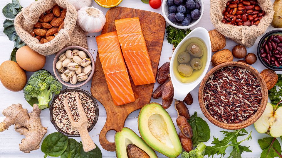 Whole foods including salmon, avocado, nuts, beans, eggs and vegetables on a table